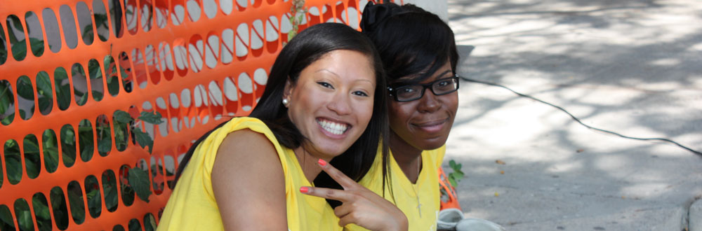 Smiling Osgoode students sitting by orange fence in yellow t-shirts