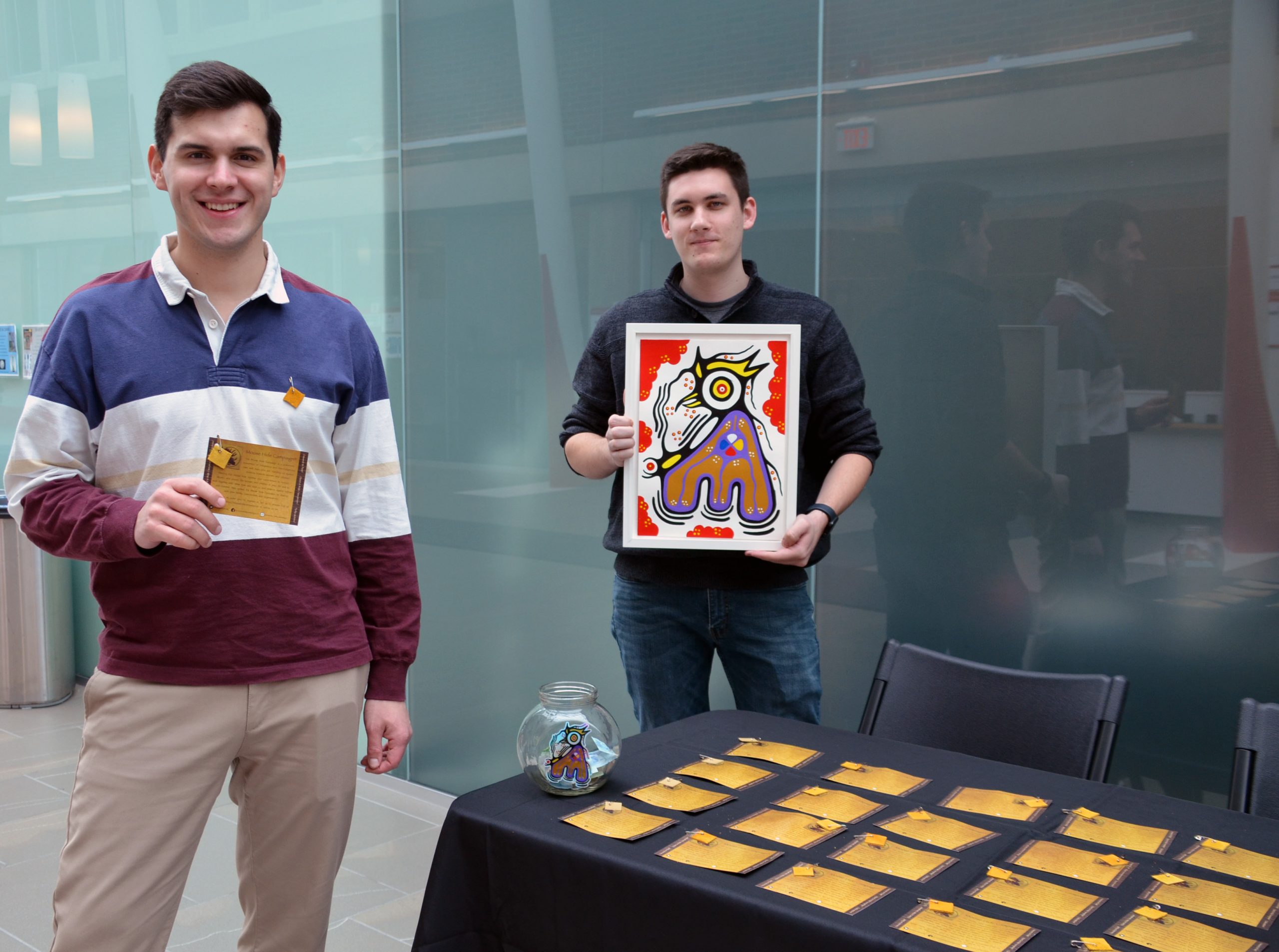 OISA exec members Levi Marshall and Justin Thompson stand next to table with Moose Hide pins